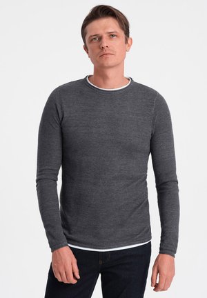 Dunkelgraues Langarmshirt mit strukturiertem Strickmuster und einem weißen gerippten Halsausschnitt, kombiniert mit dunklen Jeans.