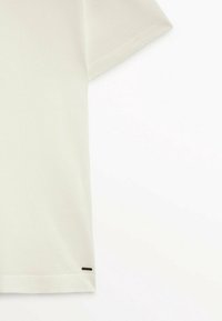 T-shirt en coton léger de couleur claire, à manches courtes, col rond et avec un petit accent noir à l'ourlet. Texture lisse.