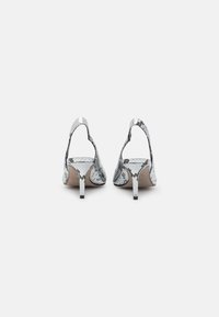 Zapatos de tacón con un diseño de estampado de serpiente en blanco y negro, con la parte posterior abierta y tacones finos. Textura suave y acentos de hardware mínimos.