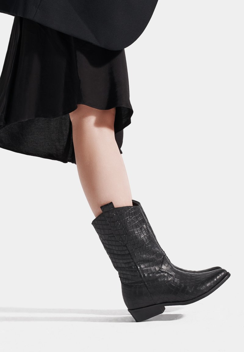Czarne ankle boots z welurowej skóry z wytłoczonym wzorem w kształcie krokodyla, z wąskim noskiem i niskim obcasem w kształcie słupka, z pętelką do zakupu i teksturowaną powierzchnią.