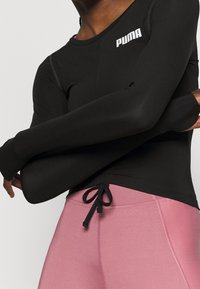 Czarna sportowa koszulka z długim rękawem z małym białym logo Puma oraz różowe legginsy do jogi z troczkiem w talii. Gładka tekstura.