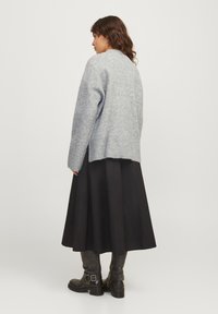 Pull en maille gris avec une coupe décontractée, ourlet côtelé, associé à une jupe midi noire et des bottes hautes noires, vu de dos.