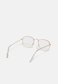 Ochelari de soare pătrați cu rame subțiri din metal roz aurit. Lentile transparente și brațele delicate cu vârfuri curbate. Design minimalist, geometric.