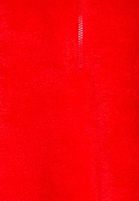 Czerwona polarowa kurtka z półzamkiem z przodu, miękka teksturowana tkanina i gładki zamek błyskawiczny. Jasny, jednolity kolor bez widocznych wzorów.