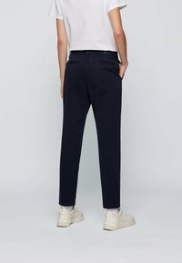 Granatowe chinosy o dopasowanym kroju, wykonane z miękkiej bawełny, z dwoma tylnymi kieszeniami i bocznymi kieszeniami; stylizowane z białym t-shirtem i jasnymi sneakersami.