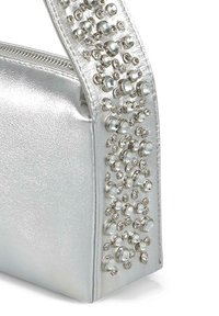 Srebrna metaliczna torebka o teksturowej powierzchni z rozrzuconymi kryształowymi zdobieniami wzdłuż paska, dodającymi głębi i wizualnego zainteresowania.
