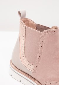 Světle růžové semišové a kožené kotníkové boty s elastickým bočním panelem, poutkem vpředu a bílou podrážkou se šedým pruhem.