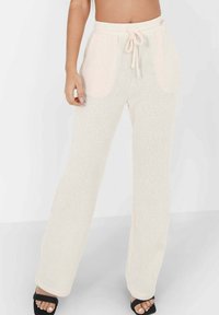 Pantalons de survêtement en tricot beige clair avec une coupe décontractée, équipés d'une taille à cordon et de poches latérales. Texture douce et design à jambes larges.