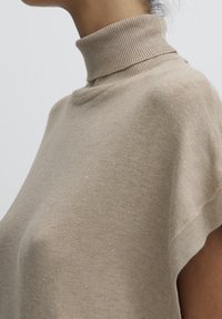 Beżowy sweter z golfem, z prążkowanym kołnierzykiem, krótkim rękawem i miękką teksturą. Prosty fason z luźnym krojem i minimalistycznymi detalami.