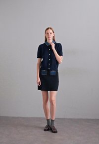 Navy short-sleeve top with knitted texture, denim accents on pockets, paired with a ribbed black skirt. Model wears gray socks and loafers.