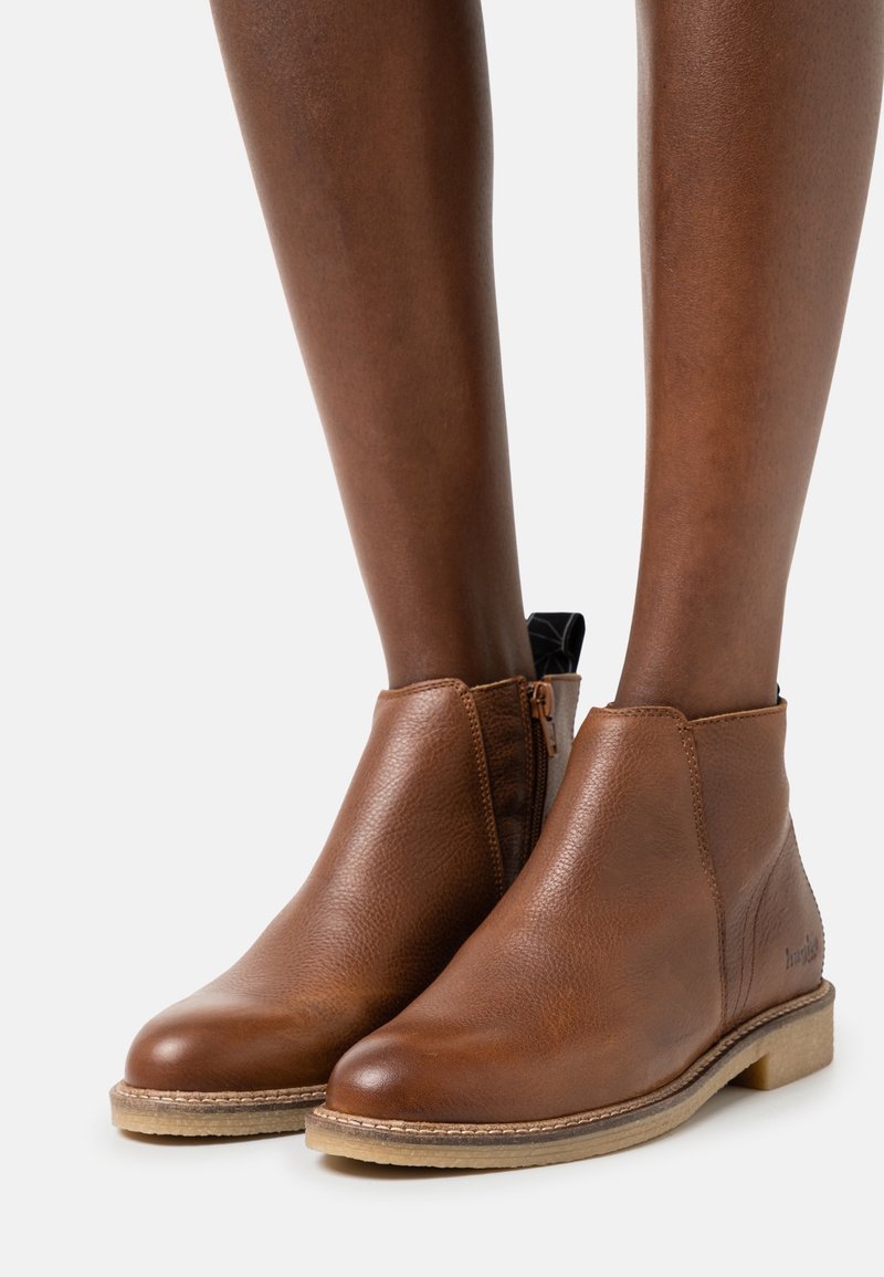 Botas de tobillo de cuero marrón con un acabado texturizado, cremallera lateral y una suela de color claro. Diseño minimalista sin hardware adicional ni patrones.