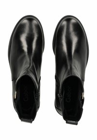 Botines de cuero negro con una textura suave, punta redonda, cremalleras laterales y sutiles detalles en dorado. El interior presenta la marca.