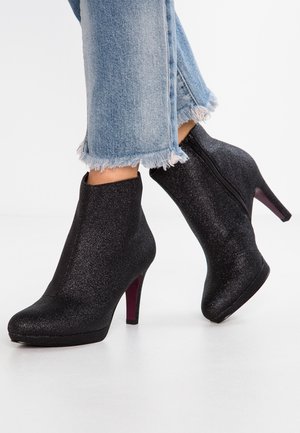 Sorte glitrende ankelstøvler med høje hæle og sidelukning, båret med lyseblå jeans med frynset kant, på en hvid gulv.