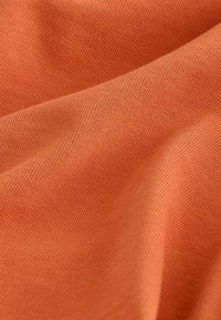 Gros plan sur un tissu orange doux et tissé avec une texture tricotée visible et des plis légers créant des ombres et des reflets.