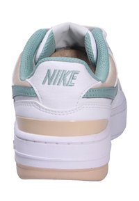 Bílé tenisky Nike s měkkou béžovou podrážkou, mentolovými akcenty a síťovinovými panely na patě. Mají logo Nike vyšitá tyrkysovou nití.