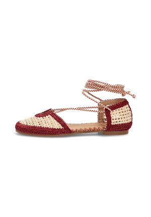 Zapato plano tejido con patrón de crochet en beige y rojo oscuro y lazos para atar en el tobillo sobre fondo blanco.