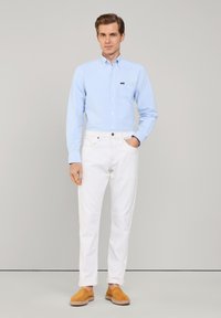 Jasnoniebieska koszula zapinana na guziki, białe proste spodnie, oraz beżowe zamszowe buty wsuwane. Prosty wzór, gładka faktura, klasyczny krój.