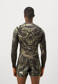 Langærmet træningstrøje og shorts i sort med grønne og gyldne grafiske mønstre, der har et kranie-design og en struktureret stoffinish.