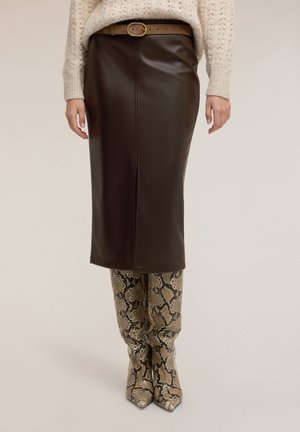 Femme portant une jupe midi en cuir marron foncé avec une ceinture marron, un pull en maille crème et des bottes montantes à imprimé serpent.