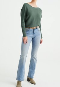 Grön räfflad långärmad topp, ljusblå utsvängda jeans med blekt textur och taupe klackade ankelstövlar. Silverbälte framhäver midjan.