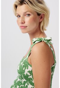 Grön och vit mönstrad klänning med smockat tyg, tunna axelband och en rosett på bandet. Slät textur.