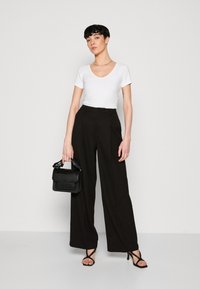 Pantalons larges noirs, haut ajusté blanc à col en V, talons noirs à lanières et petit sac à main noir texturé. Design simple et moderne.