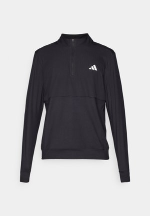 Maglia nera sportiva a zip con maniche lunghe, caratterizzata da una texture a coste e un logo riflettente bianco sul lato sinistro del petto. Presenta un colletto alto e polsini aderenti.
