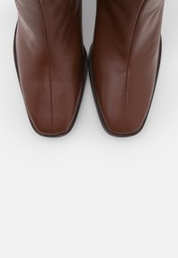 Botas de tobillo de cuero marrón con un diseño elegante, punteras cuadradas y textura suave, con una costura lateral y suelas resistentes.
