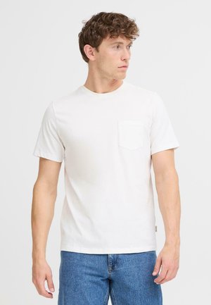 White cotton t-shirt with short sleeves, rounded neckline, and a chest pocket. Worn with blue denim jeans.