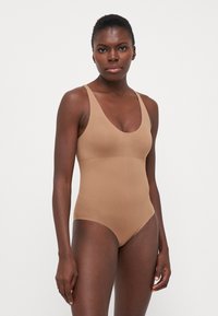 Bruine aangesloten bodysuit met brede schouderbanden en een diepe V-hals. Soepele textuur en minimalistisch ontwerp, geschikt voor zowel laagjes als om solo te dragen.
