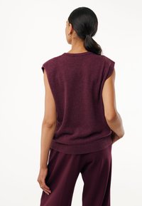 Jersey sin mangas burdeos con escote redondo y dobladillo acanalado, hecho de un material suave; combinado con pantalones holgados a juego.