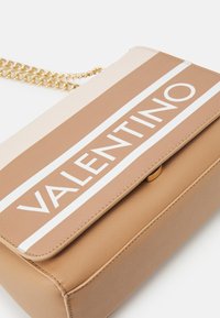 Borsa strutturata color tan con tracolla in catena dorata, caratterizzata da un design a righe crema e marroni e audace scritta bianca "VALENTINO".