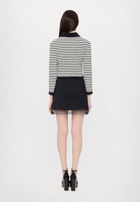 Striped knit top with a navy collar, paired with a fitted black skirt showing a sheer hem, worn with black heeled sandals.