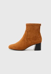 Suede enkellaars in tan met een spitse neus en een zwarte blokhak. Voorzien van elastische zijpanelen en een trekband aan de achterkant.
