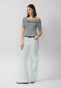 Top off-shoulder a righe bianche e nere abbinato a pantaloni ampi azzurri e una cintura blu navy, con una fibbia metallica rotonda.