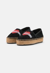 Svart mocka espadrilloskor med jutesula. Har upphöjda röda och vita bokstäver med texten "Moschino" samt en hjärtografi på framsidan.