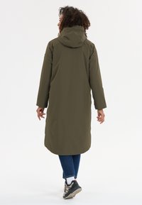 Olijfgroen waterdichte lange jas met een capuchon, gladde textuur en rechte snit, gecombineerd met donkerblauwe jeans en neutrale sneakers.