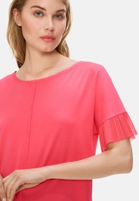 Bright pink top with short sleeves featuring pleated accents. Soft fabric and a subtle round neckline enhance its casual design.
