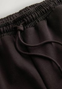 Detailní záběr na tmavě hnědý elastický pás kalhot s tkaničkou na světlém pozadí.