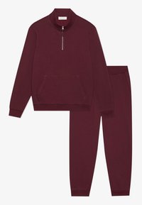 Burgundský svetr s vysokým límcem a polo zipem, s přední kapsou; odpovídající tapered kalhoty s elastickým pasem a bočními kapsami.
