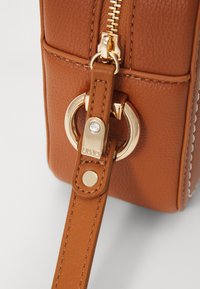 Braune strukturierte Lederhandtasche mit goldenen Beschlägen, ausgestattet mit einem Reißverschluss, einem Ringbefestigungselement und einem dekorativen Stichdetail.