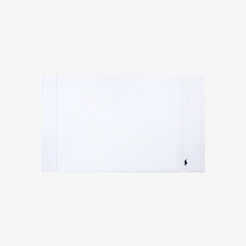 Λευκό βαμβακερό πατάκι μπάνιου με ομαλή υφή, με διπλές ραφές στα άκρα και μικρό κεντημένο λογότυπο στην κάτω γωνία.