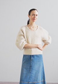 Ανοιχτό μπεζ αφράτος πουλόβερ με φαρδύ λαιμό και φουσκωτά μανίκια, συνδυασμένο με μπλε τζιν φούστα που διαθέτει ραφή μπροστά.