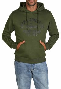 Green hoodie with a kangaroo pocket, drawstring hood, and front print logo. Fabric appears soft with a smooth texture. Paired with blue jeans.