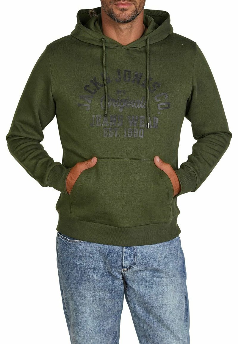 Green hoodie with a kangaroo pocket, drawstring hood, and front print logo. Fabric appears soft with a smooth texture. Paired with blue jeans.