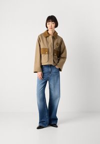 Bruine cropped jas met suède zakken, knoopsluiting en een contrasterende kraag, gecombineerd met losse blauwe spijkerbroeken en zwarte schoenen.