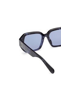 Hexagonální sluneční brýle s tmavě modrým rámem z plastu s vzorem a světle modrými čočkami. Na spánku je umístěno logo.