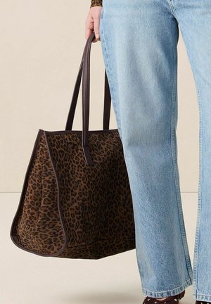 Bruine luipaardprint tote bag met donkerbruine hengsels, met een gestructureerde vorm en een gladde textuur. Draagt bij lichte blauwe jeans.