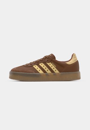 Brown suede sneaker met gouden drie strepen, gestructureerde beige accenten, rubberen zool en sterpatroon details langs de zijkant.
