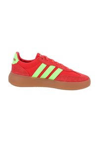 Red Adidas sneaker with neon green stripes, suede accents, and a gum rubber sole viewed from the side.